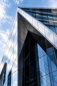 Modern glass office tower seen from below against a blue sky